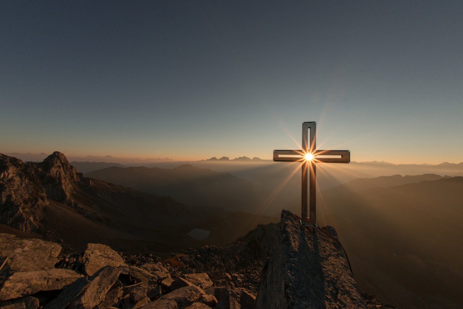 A photo of a hill top cross with rising sun